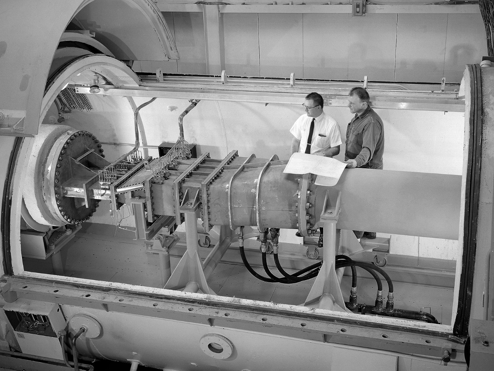 Engineer Frank Kutina and a mechanic examine the setup of an advanced combustor rig inside one of the test cells